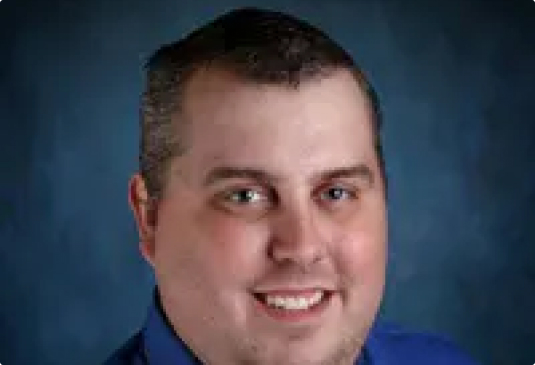 Smiling person in blue shirt, blue background.