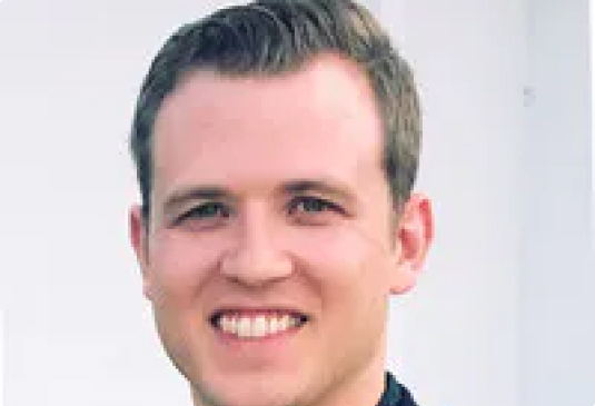 Smiling person with short hair in a light background.