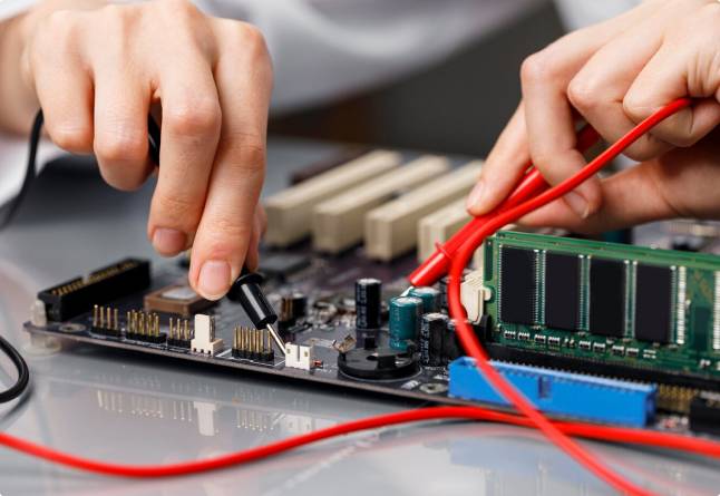 Hands using probes on a computer motherboard.