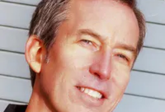 Smiling man with gray hair against striped background.