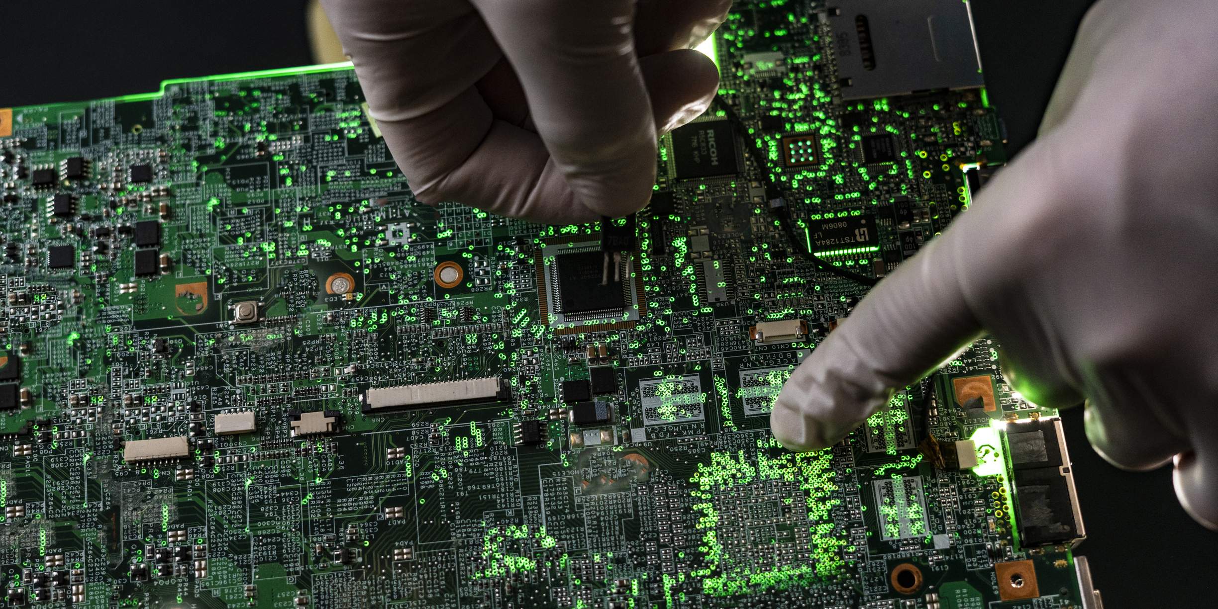 Gloved hands working on a circuit board.